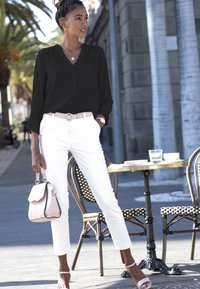 Zwarte blouse met een V-hals en knopen, witte strakke broek, roze riem en kleine handtas. Glad textuur en eenvoudig kleurenpalet.