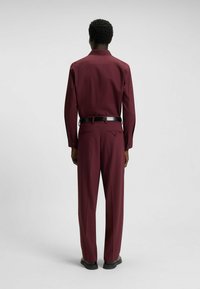 Maroon button-up shirt with long sleeves and back yoke detail, paired with matching trousers, slim fit, and black belt. Smooth fabric texture.