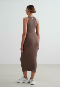 Brown ribbed sleeveless dress, mid-calf length, showcasing a fitted design, paired with white sneakers. Knit texture, minimalist branding detail on back.