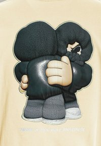 Camiseta de tela beige con un gráfico en relieve de dos figuras abrazándose con ropa negra, con detalles texturizados y acentos en blanco abajo.