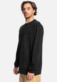 Černé tričko s dlouhým rukávem vyrobené z bavlny, s náprsní kapsou a logem, kulatým výstřihem a volným střihem.