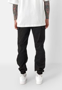 Zwarte cargobroek met elastische boorden, voorzien van zijzakken, gecombineerd met witte sneakers. Model draagt een losvallend wit T-shirt.