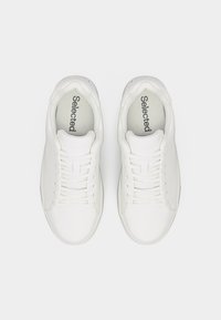 Ζευγάρι λευκά αθλητικά παπούτσια με κορδόνια και επενδύσεις εσωτερικά με την επωνυμία "Selected", εμφανιζόμενα από πάνω σε απλό λευκό φόντο.