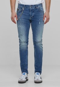 Világoskék, slim fit farmernadrág, kopott hatással, ezüst lánccal, amely a derékszíjhoz csatlakozik.