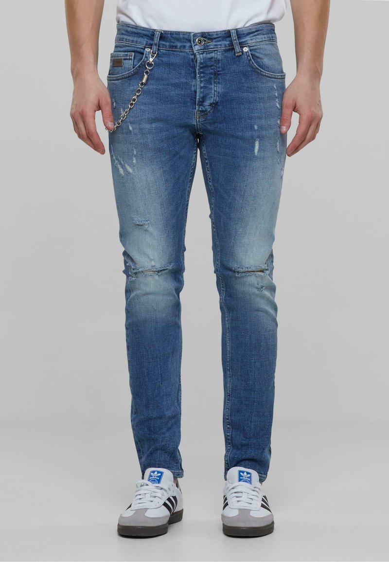 Világoskék, slim fit farmernadrág, kopott hatással, ezüst lánccal, amely a derékszíjhoz csatlakozik.