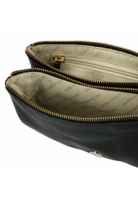 Funda de cuero negro con dos compartimentos con cremallera, herrajes en tono dorado y un interior de color beige claro que presenta un patrón de marca repetido.