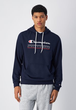 Marineblauwe hoodie met een voorste kangoeroezak, witte trektouwen en het logo "Champion ATHLETIC WEAR" in rood en wit. Zachte katoenmix stof.