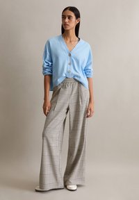 Jasnoniebieski dziergany kardigan z dekoltem w serek i złotymi guzikami, zestawiony z szerokimi spodniami w kratę w neutralnych odcieniach oraz białymi trampkami.