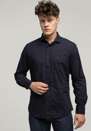 Granatowa koszula z długim rękawem ozdobiona małym białym wzorem w kropki, z kołnierzykiem zapinanym na guziki, kieszenią po lewej stronie klatki piersiowej oraz gładką fakturą.