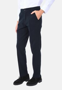 Chino blu navy in cotone misto, con frontale piatto, tasche laterali e chiusura a un solo bottone. Abbinati a scarpe in suede nere.