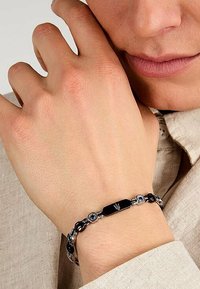 Metallarmband med svarta länkar, blå accenter och en central svart rektangulär del med en logotyp. Slät yta och elegant design.