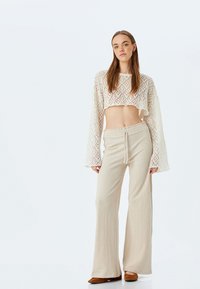 Gehaakte cropped top in crème met brede mouwen, gecombineerd met loszittende beige broeken met een elastische tailleband. Bruine platte schoenen.