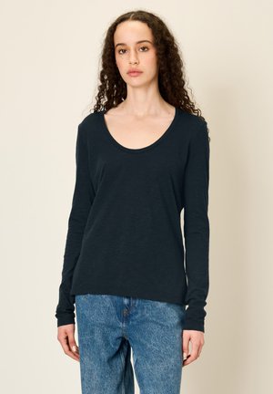 Long-sleeve black T-shirt made of soft fabric with a scoop neckline, displayed with light blue denim jeans.