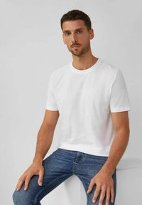 Camiseta blanca de algodón con cuello redondo clásico y mangas cortas, combinada con jeans de mezclilla azul. Textura suave y diseño minimalista.