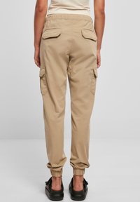 Beżowe spodnie cargo z elastycznym pasem, bocznymi kieszeniami i elastycznymi ściągaczami przy kostkach, wykonane z lekkiego materiału.