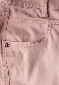 Vaaleanpunainen puuvillakangas, jossa on sivutasku mustalla metallinapilla ja kontrastiväreillä ommeltuna, esittelee sileän pinnan ja rentoa muotoilua.