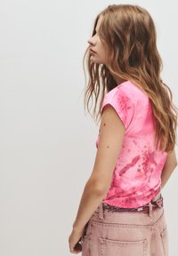 Lyserød tie-dye kortærmet top med ribbet struktur, der har en buet halsudskæring og en afslappet pasform, parret med lyserøde high-waisted jeans.