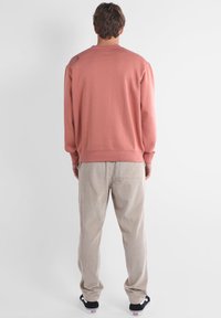 Sweat-shirt rose poussière à manches longues avec ourlet et poignets côtelés, associé à un pantalon en velours côtelé beige clair et des baskets noires.