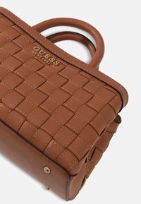 Sac à main tressé marron avec une texture lisse, présentant un logo, des poignées arrondies et des accents de ferrures dorées.