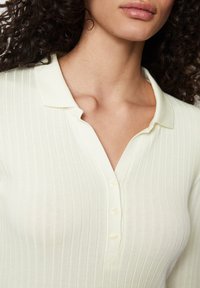 Polo shirt rigato di colore giallo chiaro, con colletto e tre bottoni. Il tessuto sembra morbido con una leggera lucentezza.