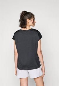 T-shirt nera a maniche corte con vestibilità rilassata, caratterizzata da una texture liscia e un collo rotondo, abbinata a pantaloni corti grigio chiaro.