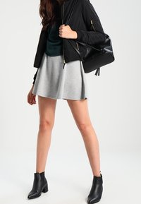 Veste bomber noire, haut bleu sarcelle, jupe évasée grise et bottines noires. La tenue présente une texture lisse et un design minimaliste.