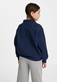 Marinblå tröja med struktur i klassisk krage, avslappnad passform och ribbade muddaramar, kombinerad med ljusgrå byxor.