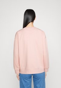 Sudadera rosa de corte relajado, con puños acanalados y escote redondo. Llevada sobre unos vaqueros azules, con una textura suave y un diseño minimalista.