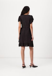 Vestido preto com padrão floral, mangas curtas e leques, cintura ajustada e bainha com babados. Par de saltos pretos de tiras traseiras.