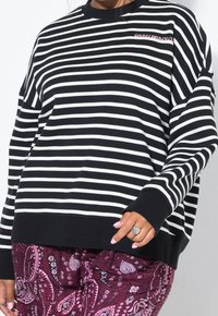 Sweat-shirt rayé noir et blanc avec un col rond, une coupe décontractée et des poignets côtelés. Présente le texte « SUNDAY BRUNCH » brodé en rose.