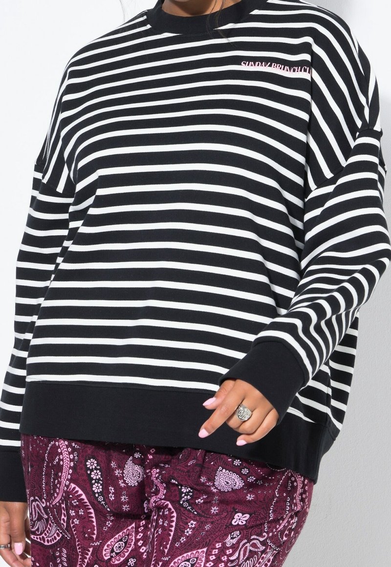 Sweat-shirt rayé noir et blanc avec un col rond, une coupe décontractée et des poignets côtelés. Présente le texte « SUNDAY BRUNCH » brodé en rose.