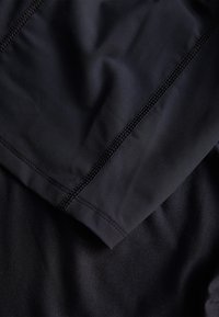 Tejido atlético negro en capas, con una textura suave y detalles de costura reforzada a lo largo de los bordes, sin patrones o acentos visibles.