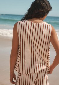 Striped sleeveless top and matching pants in cream with rust vertical stripes, made from textured fabric, view from the back at the beach.