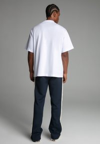 White cotton t-shirt and navy sweatpants with side white stripes. The pants have a relaxed fit and the t-shirt has a standard crew neck.