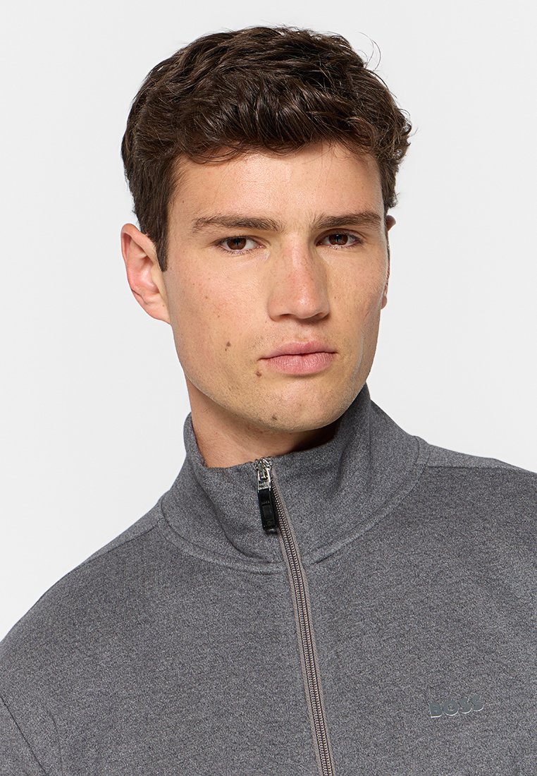 Grijze, zip-up sweater met een hoge kraag, gemaakt van textuurstof, met een subtiele logo op de borst en een strak ontwerp.