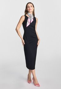 Czarna sukienka bez rękawów o dopasowanej sylwetce, w zestawieniu z białą i różową szalą w wzory oraz różowymi szpilkami. Gładka tekstura materiału.