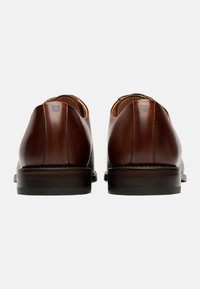 Chaussures en cuir marron avec une texture lisse, une forme arrondie et un talon bas. Présentent des coutures subtiles et une finition polie.