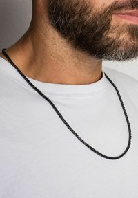 Colier din lanț de metal negru așezat pe un gât, având o textură netedă și un design răsucit, purtat cu un tricou alb simplu.
