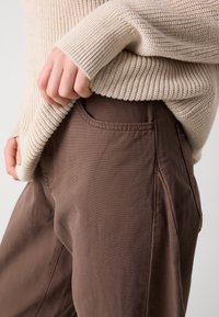 Beige stickad tröja med ribbat mönster, kombinerad med bruna, släta byxor i tyg med sidfickor och en avslappnad passform.