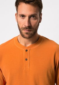 Oranje henleyshirt met lange mouwen en een gestructureerde afwerking, voorzien van drie zwarte knopen en een ronde kraag. Eenvoudig, getailleerd ontwerp.