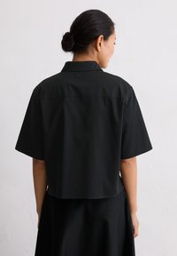 Maglietta nera a maniche corte con colletto, realizzata in tessuto liscio. Presenta un design cropped e una silhouette pulita e semplice senza decorazioni.
