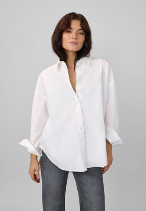 White button-up shirt with a loose fit, rolled sleeves, and light blue buttons. Paired with dark gray jeans. Smooth, lightweight fabric.