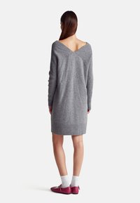 Šedé pletené šaty s véčkovým výstřihem na zádech, dlouhými rukávy a žebrovaným lemem. Spárované s růžovými botami a bílými ponožkami.