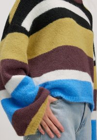 Mehrfarbiger Strickpullover mit horizontalen Streifen in Schwarz, Weiß, Gelb, Braun und Blau. Weicher Stoff mit weiten Ärmeln.