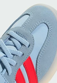 Ljusblå sneakers i mjuk mocka och nylonmaterial, med röda ränder, platta snören och en texturerad gummisula.