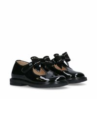 Scarpe in pelle verniciata nera con punta arrotondata, caratterizzate da una fascetta e un grande fiocco decorato con borchie nella parte anteriore. Design con suola piatta.