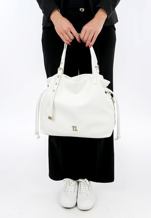 Sac à main en cuir blanc avec des accents en métal doré, double poignée et fermeture à cordon. Présente un logo à l'avant et une texture lisse.