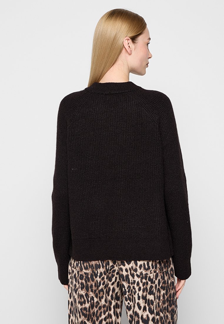 Maglione nero lavorato a maglia con scollatura a girocollo, maniche raglan e orlo a coste. La trama è spessa, abbinata a pantaloni a stampa animale.