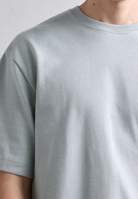 Světlá šedá krátká rukávová tričko vyrobené z bavlny. Má kulatý výstřih a hladkou texturu s jemnými detaily šití.