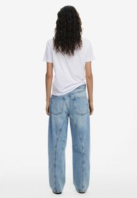 Hellblaue, weit geschnittene Jeans aus Denim mit einem klassischen Fünf-Taschen-Design und gekrümmten Nahtdetails, kombiniert mit einem weißen T-Shirt.